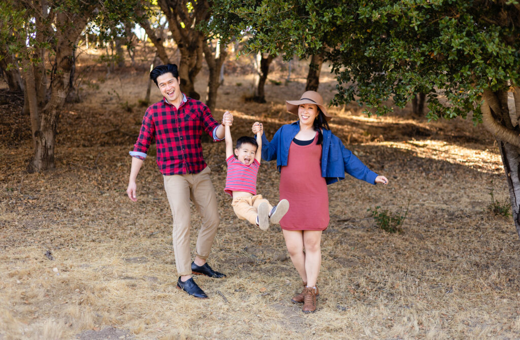 Parents swinging their child under the trees at a park