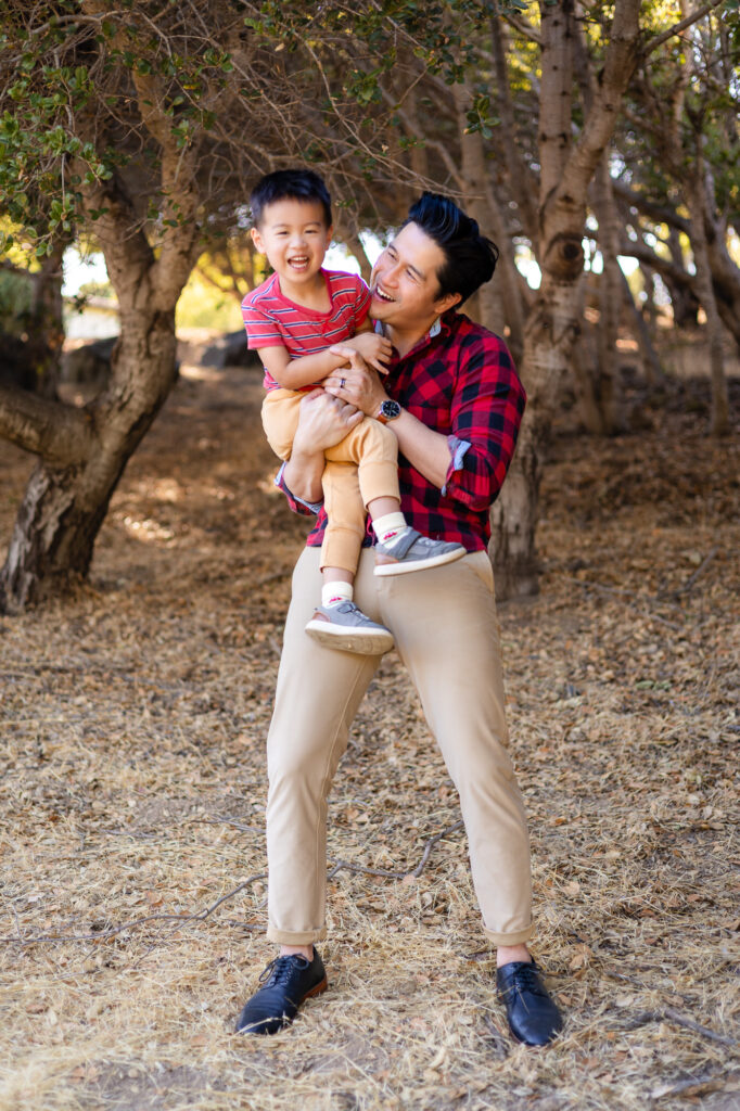 Dad lifting son and laughing together at open grassy areas in San Mateo