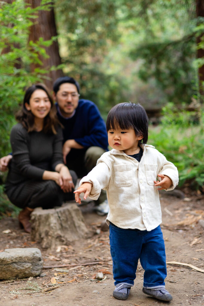 Toddler walking toward camera with parents in background at Redwood Grove Los Altos – Ellobelle Photography