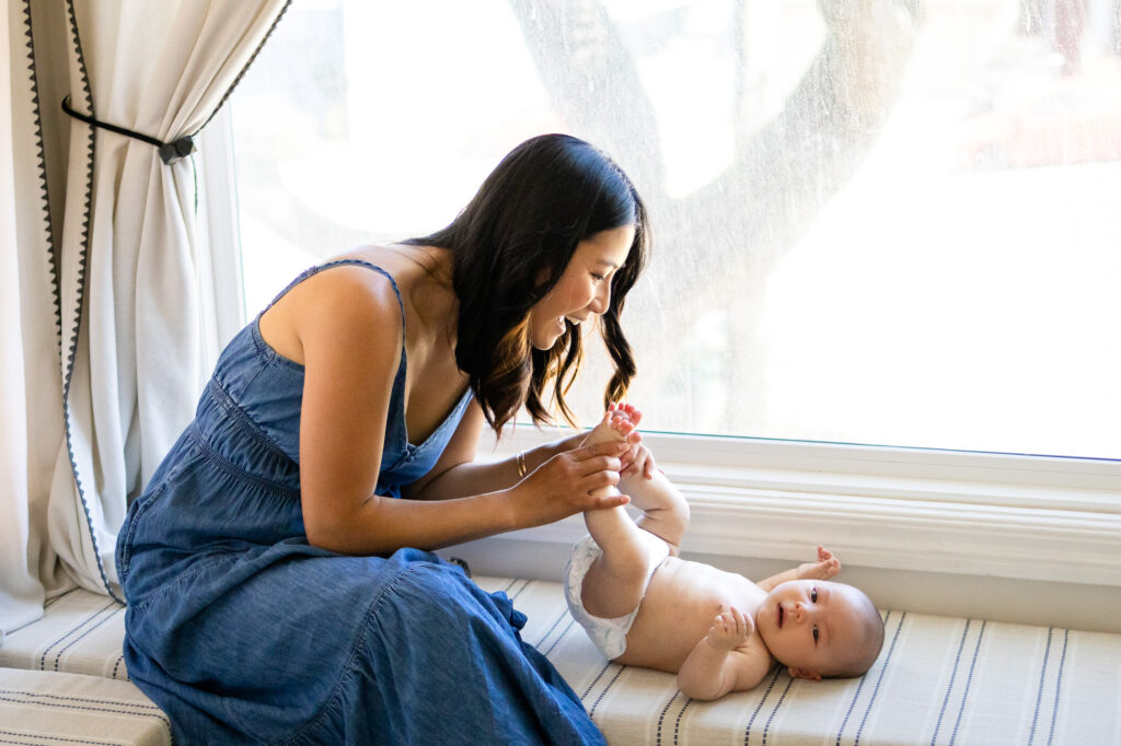 Playful mom holding baby’s feet by window – San Francisco Newborn Photography by Ellobelle Photography