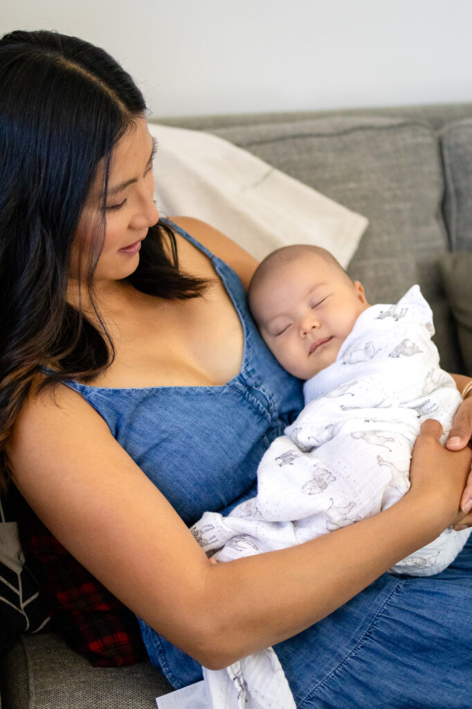 Newborn peacefully sleeping in mom’s arms on the couch – San Francisco Newborn Photography by Ellobelle Photography