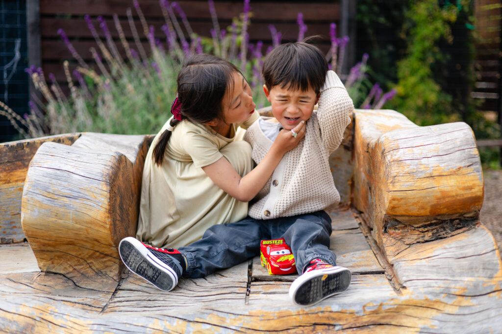 Sister hugging her little brother on a wooden bench at Washington Park Burlingame – Ellobelle Photography