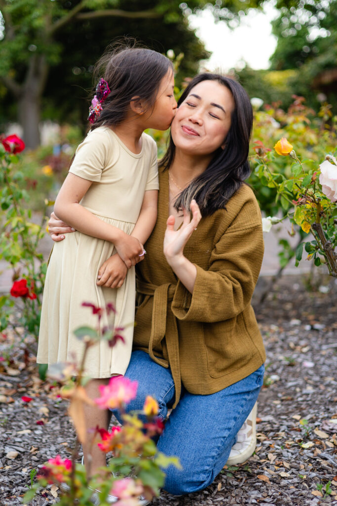 Daughter kissing mom on the cheek in flower garden at Washington Park Burlingame – Ellobelle Photography