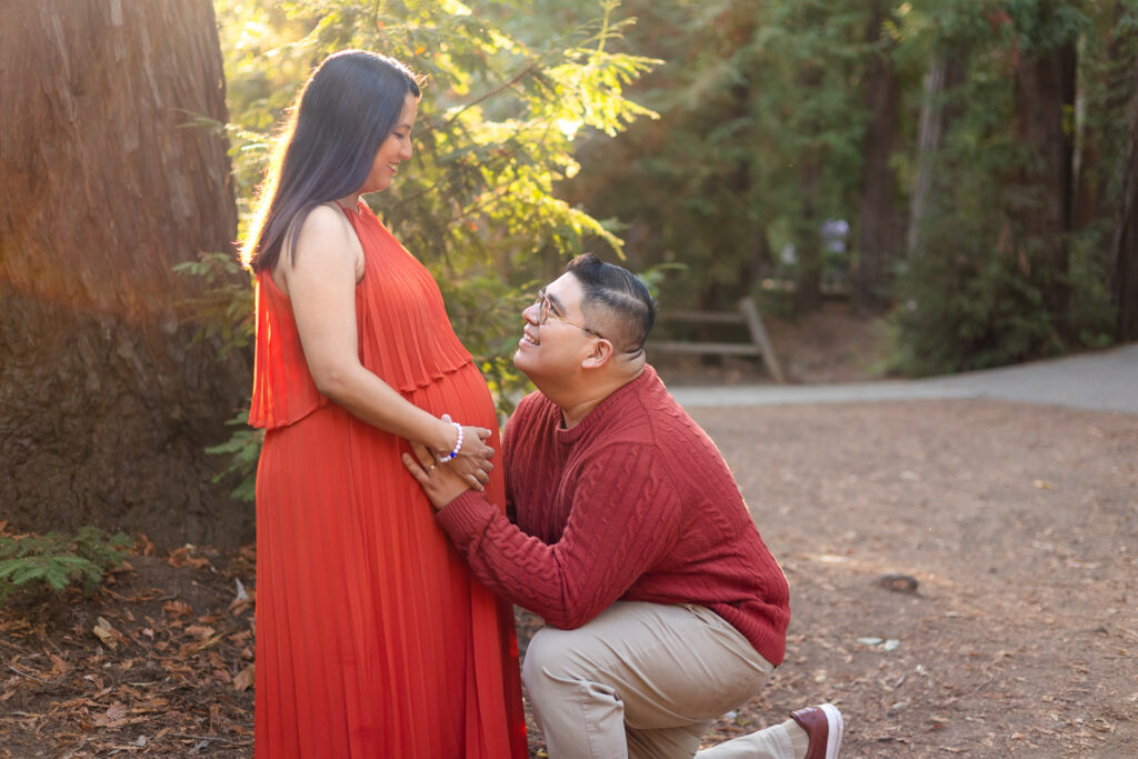 Dad kneeling to kiss baby bump during golden hour in redwood grove los altos