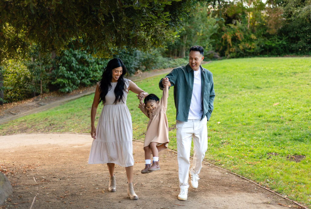 Parents swinging daughter while walking through the park during holiday photo session – Ellobelle Photography
