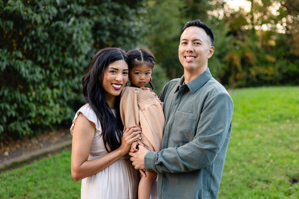 Parents posing with daughter in grassy park setting for holiday photo sessions – Ellobelle Photography