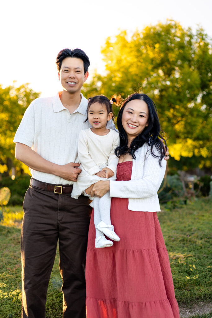 Smiling family standing together in the golden light at Leo Ryan Park