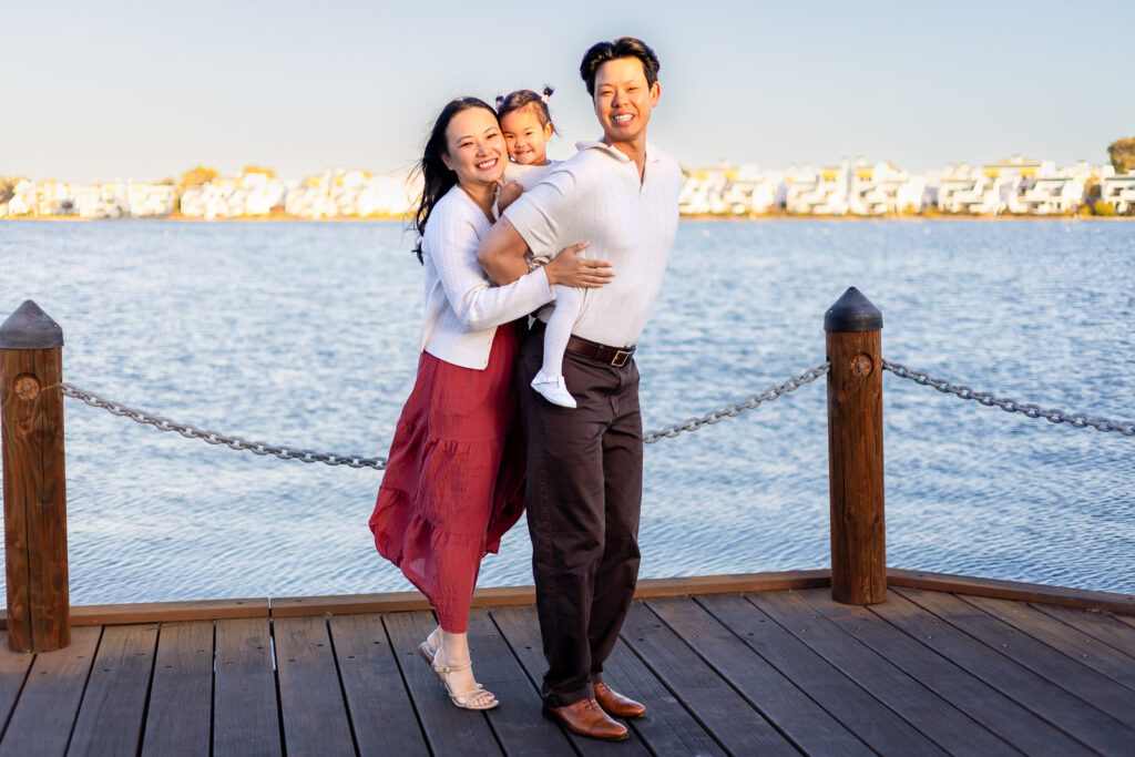 Smiling family hugging by the water at Foster City Bayfront park