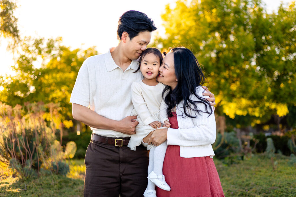Parents kissing their daughter during sunset