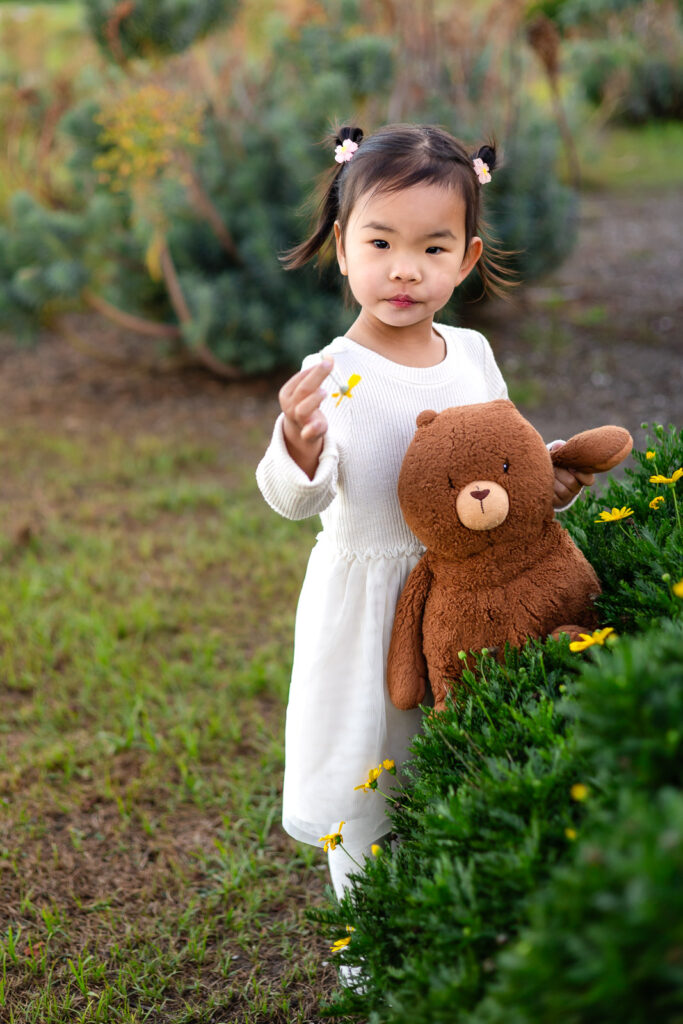 Girl holding a teddy bear and flower by the shrubs at Foster City Bayfront park