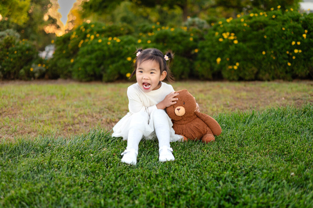 Toddler laughing on the grass with teddy bear at open lawns near the Foster City lagoon