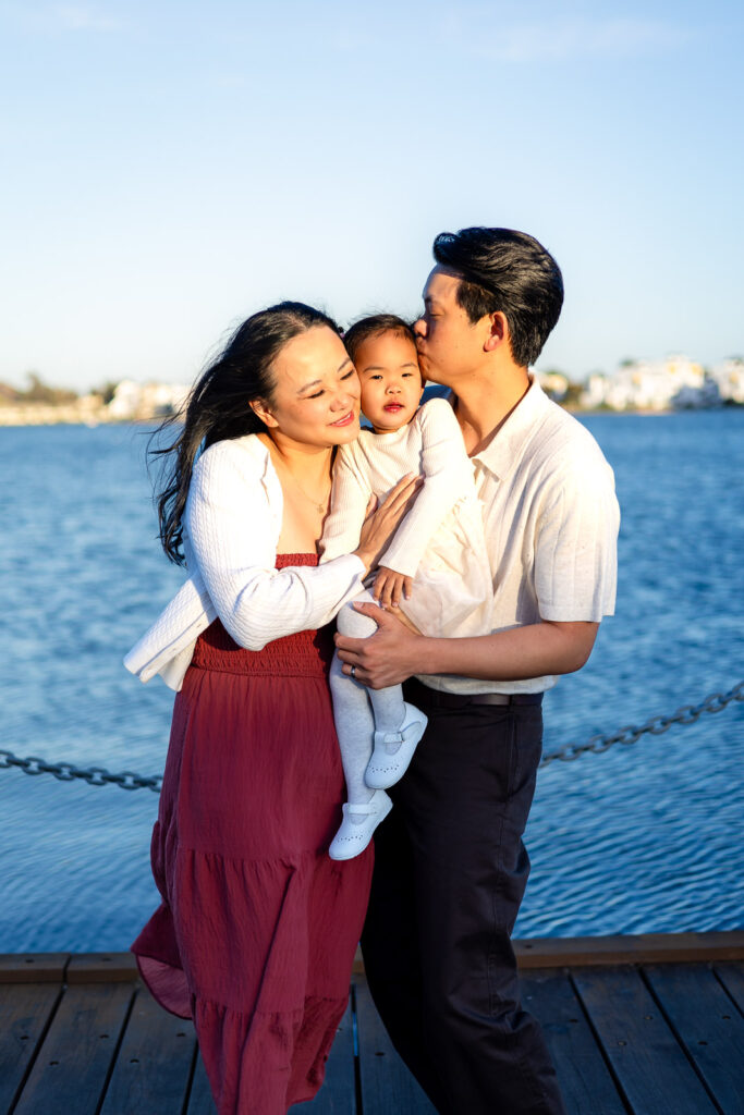 Parents cuddling their daughter by the water along the waterfront in Foster City