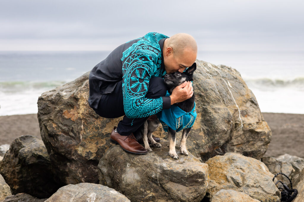 Man cuddling his dog on beach rocks