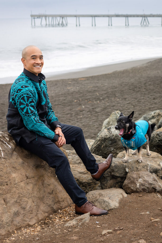 Man sitting on a rock as his dog stands nearby mid-yawn during a Peninsula dog friendly photoshoot