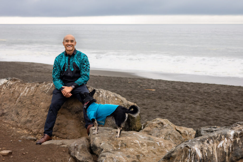 Smiling man seated on a rock with his dog looking up at him during a dog friendly family session