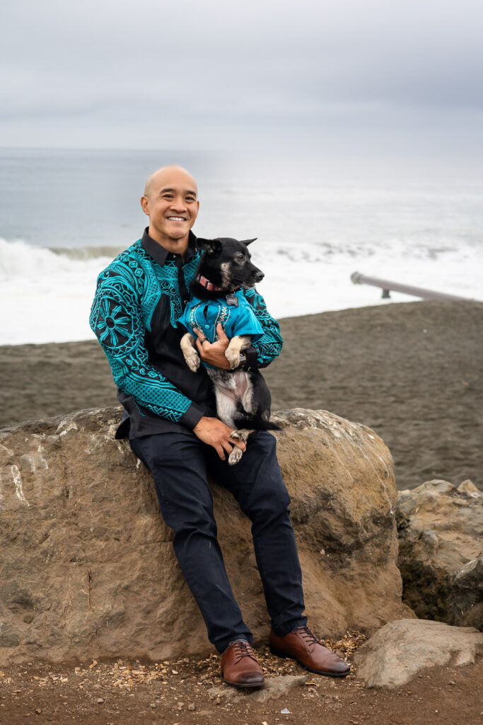 Man smiling while holding his dog on a rock near the waves bringing your dog to your session