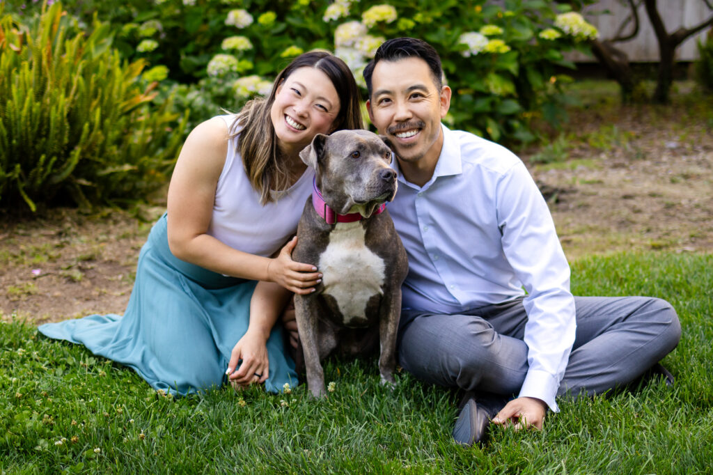 Smiling couple posing with their dog in a garden setting during photo session with dog