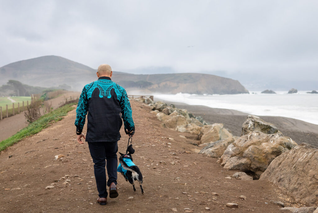 Man and dog walking down coastal path with dramatic cliffs and waves while including your dog in family photos