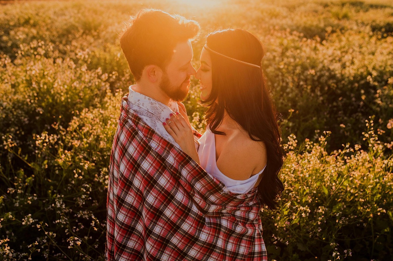 Couple wrapped in a plaid blanket at golden hour in a wildflower field, captured by an online dating photographer in the San Francisco Bay Area.