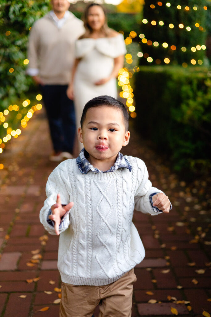 Toddler running toward the camera with holiday lights behind him during Christmas photos at Filoli