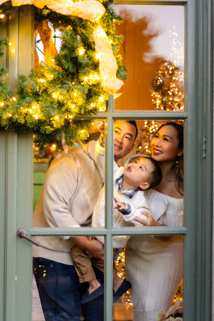 Family admiring holiday wreath lights through the Garden House window showing candid Christmas moment in the Filoli gardens