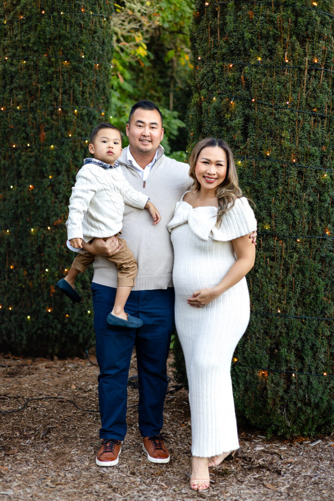 Family standing between lit evergreens at Filoli during their Filoli Christmas Photos session