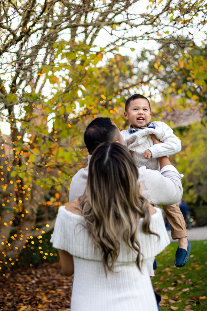 Parents holding toddler under holiday lights during Filoli Christmas Photos at Filoli Estate – Ellobelle Photography