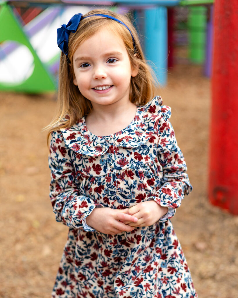 Child standing beside a bright red post at Millbrae Nursery School playground during picture day Ellobelle Photography