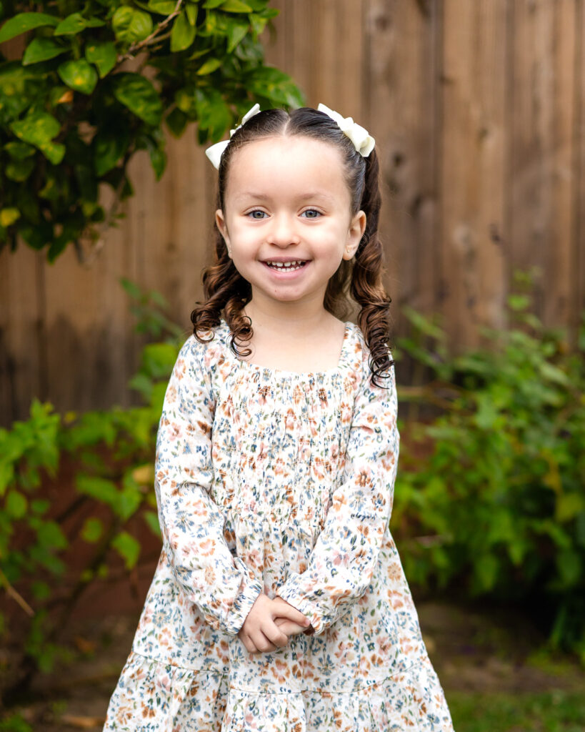 Young girl smiling in the garden area at Millbrae Nursery School during school photos Ellobelle Photography