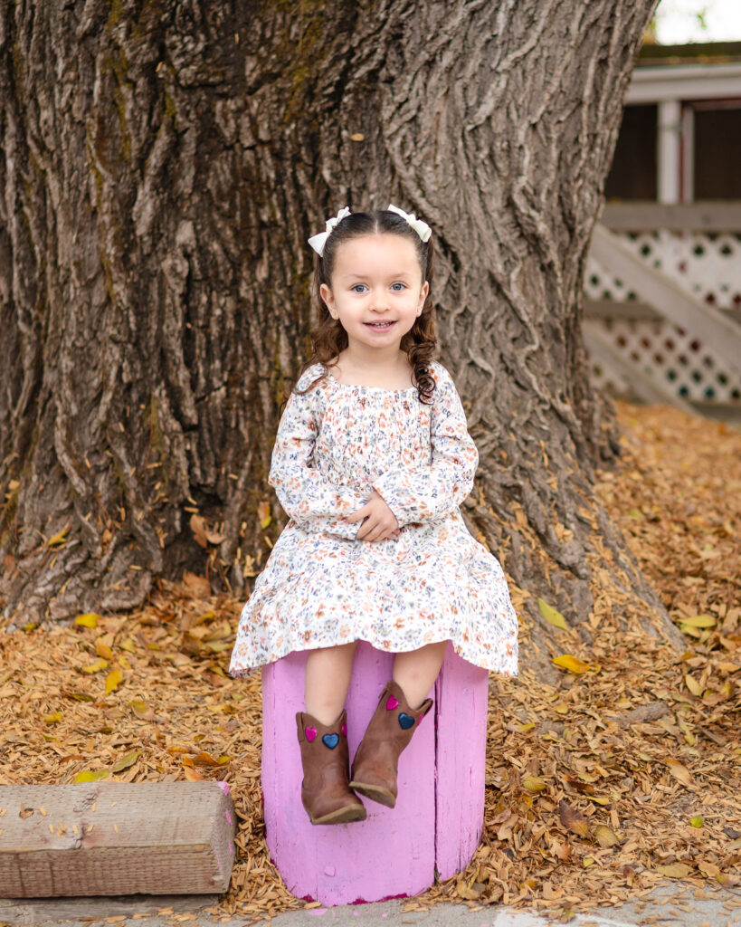 Child sitting on a pink play stump near the big tree at Millbrae Nursery School Ellobelle Photography
