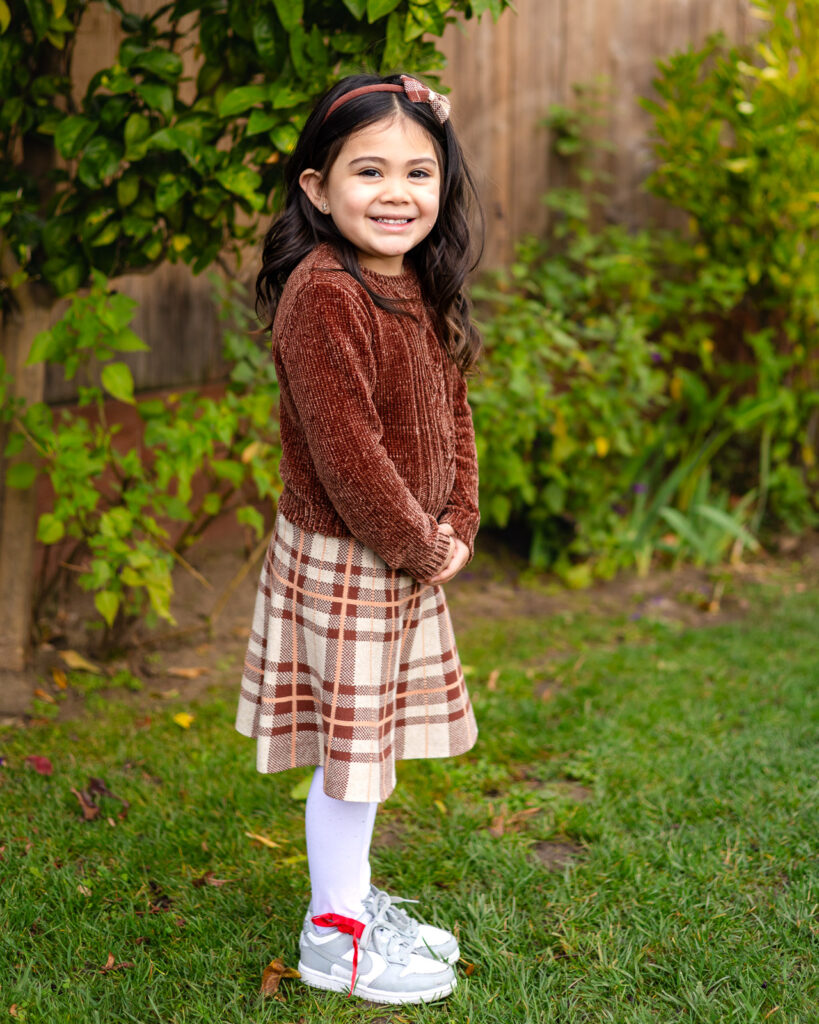 Girl smiling in the garden space at Millbrae Nursery School during fall picture day Ellobelle Photography