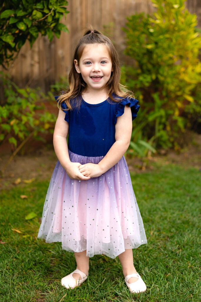 Child in a blue and pink dress smiling in the garden at Millbrae Nursery School Ellobelle Photography