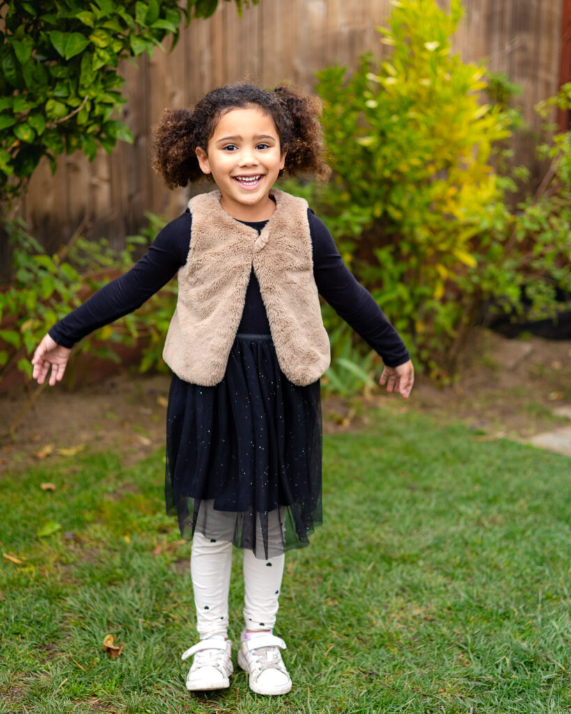 Girl smiling with arms open in the grassy yard at Millbrae Nursery School Ellobelle Photography
