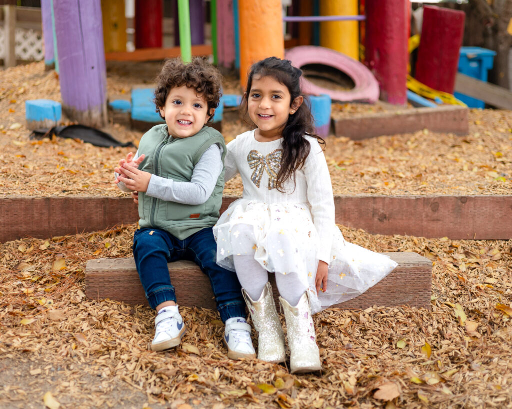 Two young children sitting on wooden steps surrounded by fall leaves at Millbrae Nursery School Ellobelle Photography