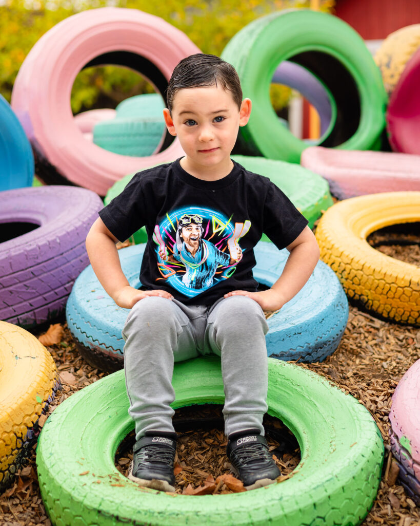Child sitting on painted green tire at Millbrae Nursery School during outdoor picture day Ellobelle Photography