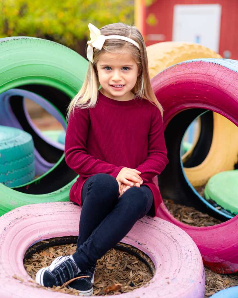 Young girl sitting on colorful painted tires at Millbrae Nursery School outdoor playground Ellobelle Photography