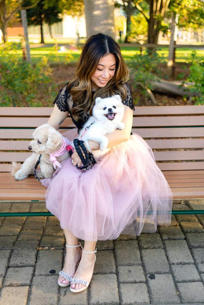 Woman seated on a park bench holding two smiling dogs for portraits