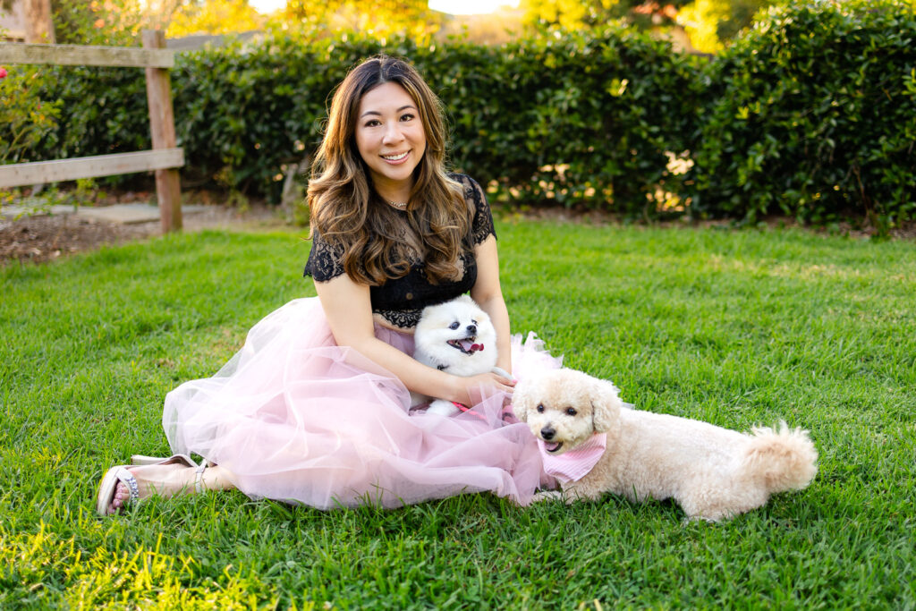Woman holding two happy dogs while seated in a green space by a San Francisco Dog Photographer