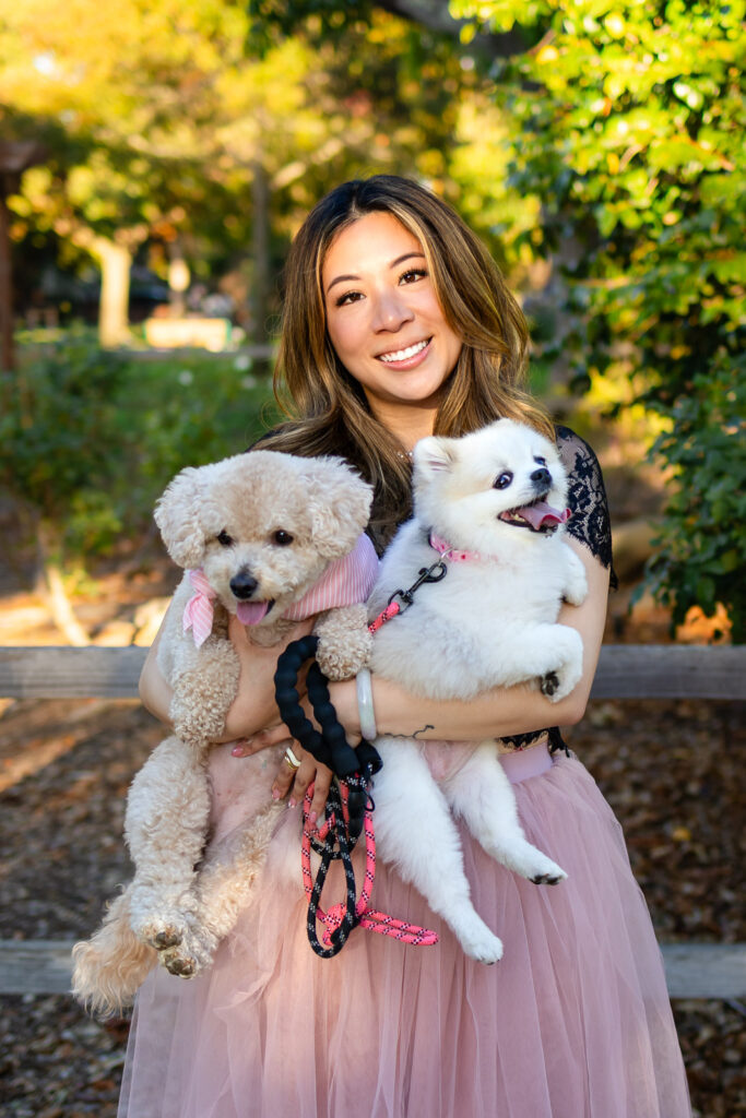 Woman posing with two fluffy dogs near a shaded garden area with a dog photographer 