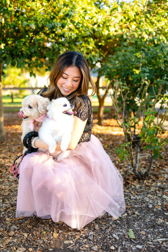 Woman holding two playful dogs in a garden area with warm sunset light by dog photographer in San Francisco
