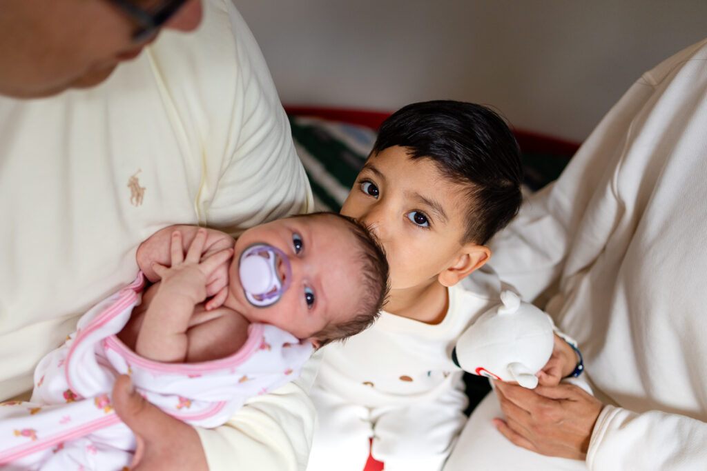 Big brother kissing his newborn sibling during a cozy in home San Mateo session with support for new moms in the Bay Area