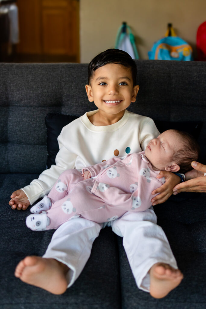 Big brother holding his newborn sibling during an in home San Mateo newborn session with support for new and expecting parents in the Bay Area