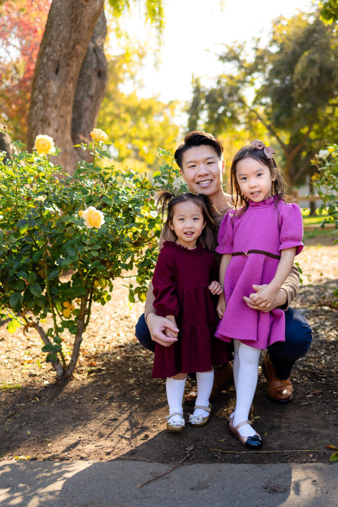 Dad kneeling with his daughters by yellow roses in a park for Family Photoshoot Tips