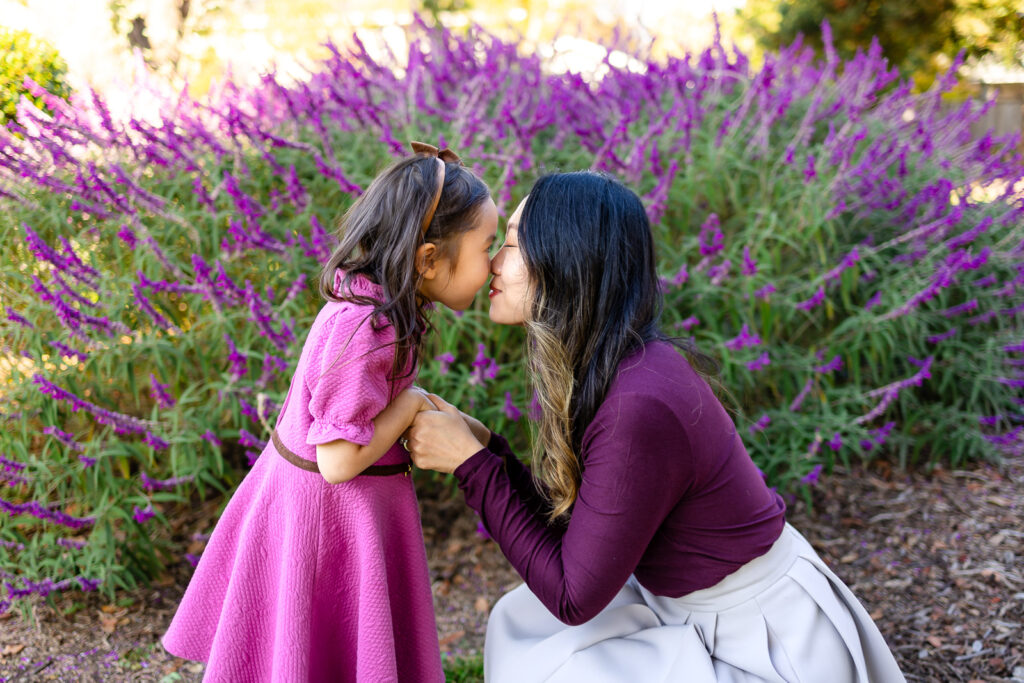 Mom and daughter sharing a sweet forehead touch near purple blooms in a how to feel comfortable during family photos session