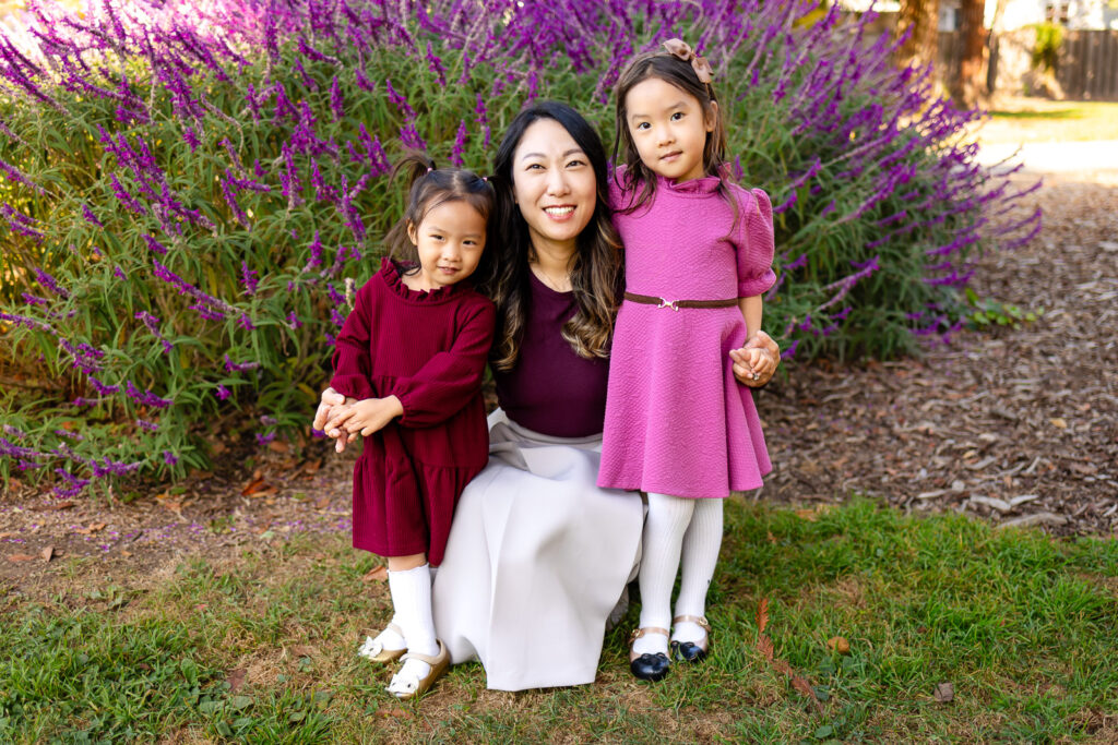 Mom smiling with her two daughters in front of bright purple flowers in a garden for Family Photoshoot Tips