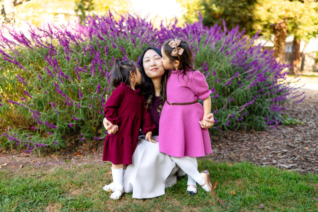 Daughters kissing their mom on the cheeks in a garden