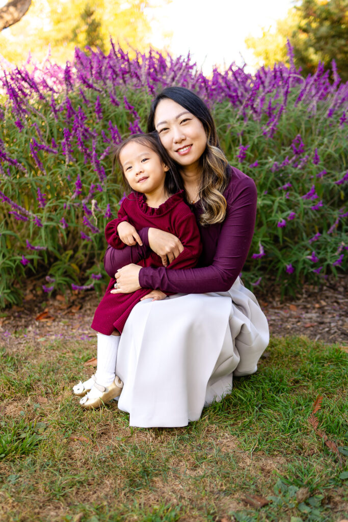 Mom holding her younger daughter near purple flowers in a garden for family photo tips