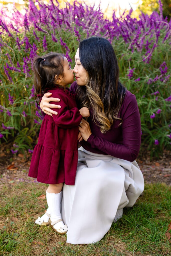 Mom and daughter sharing a sweet kiss in a garden with purple flowers for what parents should know before a session