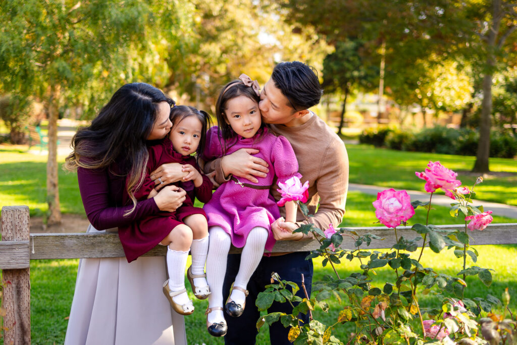 Parents kissing their daughters during a playful prepping for your family session moment in a park
