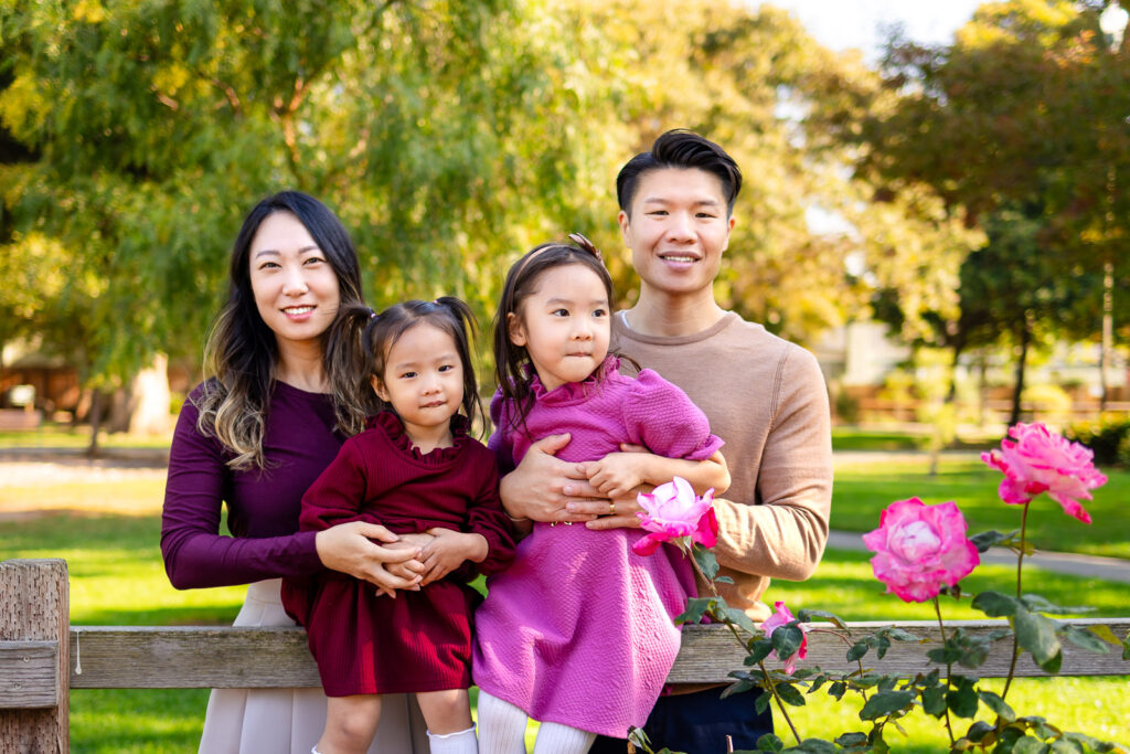Family smiling by pink roses in a garden scene for how to get your kids ready for photos